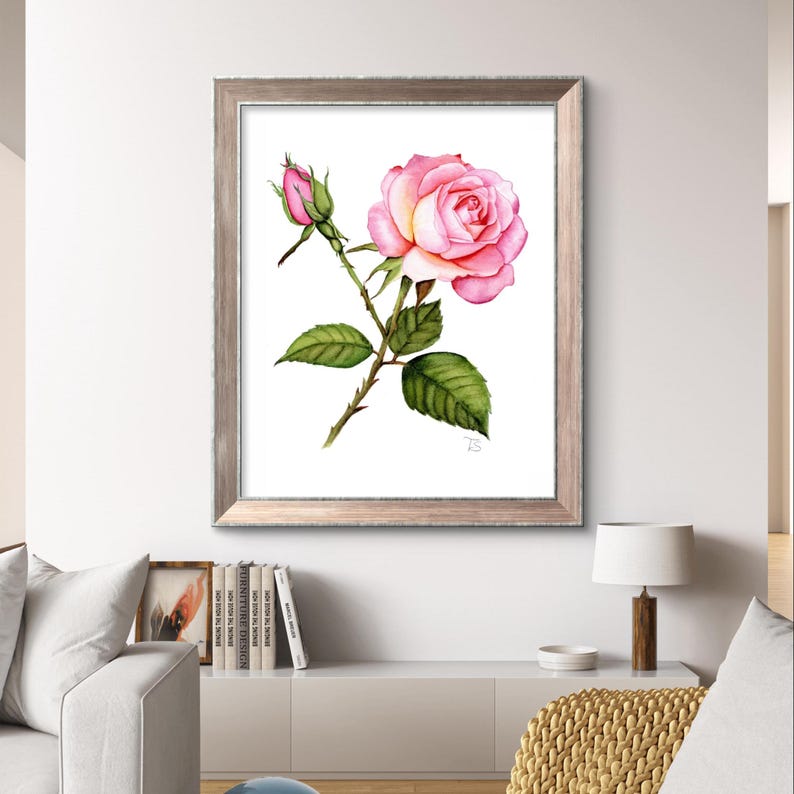 A realistic hand-painted watercolor of a delicate rose, featuring soft, blended hues of pink, yellow and green. The painting is displayed in an elegant wooden frame with a rich, warm finish that complements the softness of the artwork.