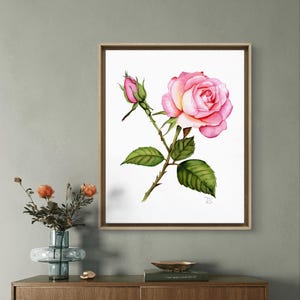 A realistic hand-painted watercolor of a delicate rose with petals gently shaded to show natural texture and depth, while the leaves are painted with fine precision. The wooden frame's simple yet stylish look enhances the overall charm of the piece.