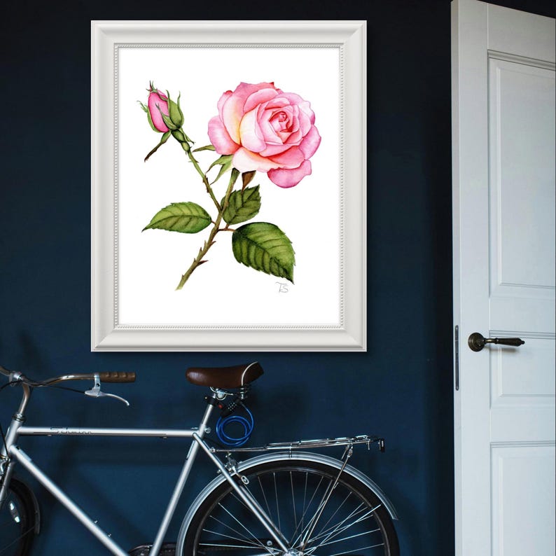 A realistic hand-painted watercolor of a rose, showcasing soft pink petals with subtle gradients of color and fine detail in the leaves. The painting is elegantly displayed in a white frame that enhances its timeless aesthetic, adding a modern touch.