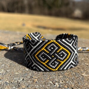 May include: Black and white friendship bracelet with a yellow geometric pattern.
