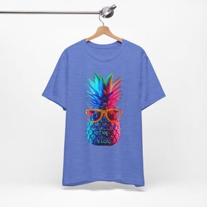 Könnte beinhalten: Ein blaues T-Shirt mit einer bunten Ananas, die eine Sonnenbrille trägt und den Text "Follow the Vibe".