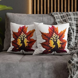 May include: Two white throw pillows with a red, orange, and yellow maple leaf design. The leaves have a silhouette of a deer inside.