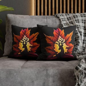 May include: Two black throw pillows with a silhouette of a deer standing in front of a large orange and yellow maple leaf. The leaves are on a black background.