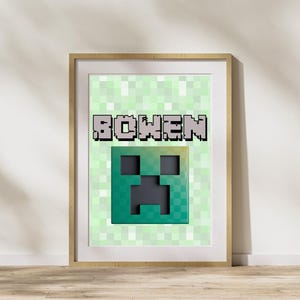 Puede incluir: Impresión enmarcada con una cara de Creeper verde y negro pixelada del juego Minecraft. El nombre "BOWEN" se muestra en letras grises pixeladas encima de la cara de Creeper sobre un fondo verde claro pixelado. La impresión está en un marco de madera.