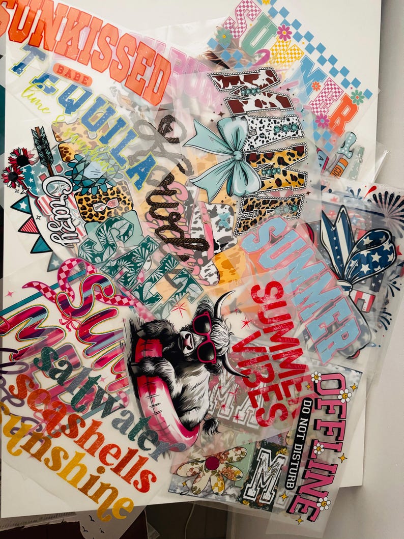 May include: A collection of iron-on heat transfer vinyl designs featuring summer-themed phrases and images. The designs include "Summer Vibes", "Sun Kissed", "Tequila", "Crazy", "Saltwater", "Seashells", "Sunshine", "Off-Line", and a Highland Cow wearing sunglasses and a float.