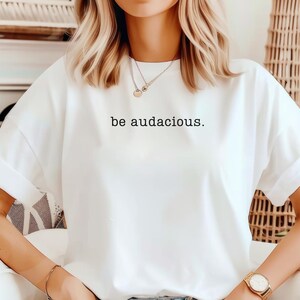 May include: White t-shirt with the text "be audacious." printed in black.