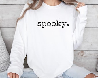 May include: A white long-sleeved sweatshirt with the word "spooky." printed in black, centered on the chest. The sweatshirt is made of a soft material and is suitable for casual wear. The design is simple and minimalist.