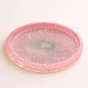 May include: A pink resin tray with a glittery, iridescent centre. The tray has a rounded oval shape with a beaded edge. The overall design is a soft, pastel aesthetic, suitable for decorative use.
