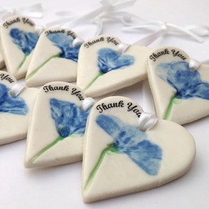 May include: A set of white ceramic heart-shaped ornaments with a blue flower design and the text "Thank You" printed on each.