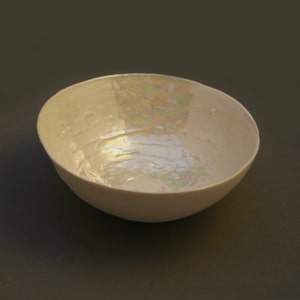 May include: A white ceramic bowl with an iridescent glaze. The bowl is oval shaped and has a smooth, rounded rim.
