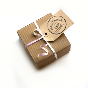 Puede incluir: Una caja de regalo marr&oacute;n con una cinta blanca y una cinta rosa. La caja tiene una etiqueta adjunta con el texto "Melissa Chorzewska Ceramics" en negro.