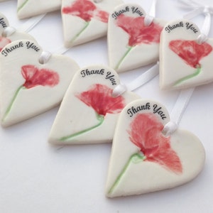 May include: A set of white ceramic heart-shaped ornaments with a red poppy flower design and the text "Thank You".