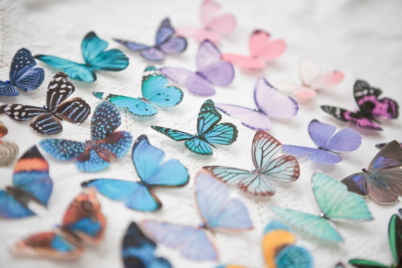 An image of a mix of pastel butterfly hair clips lined up in rows on a white vintage table cloth.