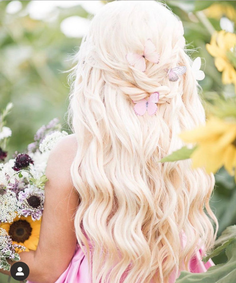 A lady with wavy long blond hair is holding a bunch of flowers including sunflowers. In the back of her hair are three pretty pale pin butterfly hair clips