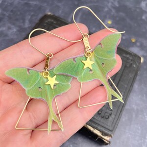 Brass triangle earrings with a green hand cut silk luna moth  and a gold star charm hanging from each earring.