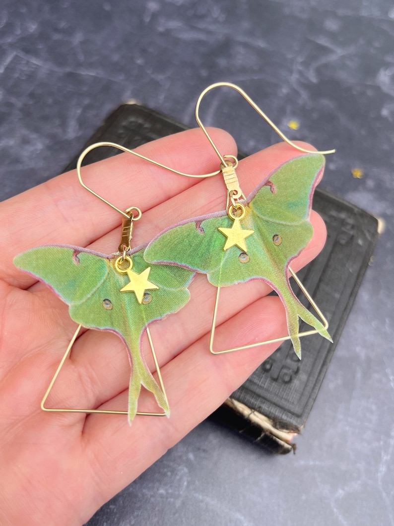 Brass triangle earrings with a green hand cut silk luna moth  and a gold star charm hanging from each earring.