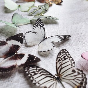 Small black and white silk butterfly hair pins rest on a neutral linen cloth. Each super realistic detailed butterfly has a tiny crystal on its head for extra sparkle.