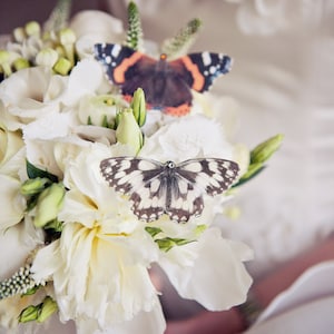 A beautiful wedding bouquet with white roses has two silk butterflies in with the flowers. A Red Admiral and a marbled white