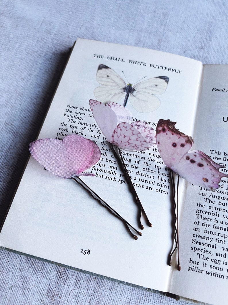 Perfect wedding hair accessories, 3 palest pink butterfly hair pins sit on an opened vintage butterfly book. These butterflies have their wings folded and are super realistic, it looks like real butterflies have landed in your hair!