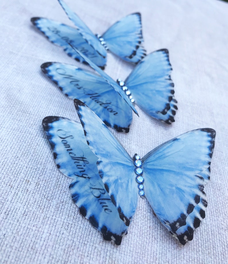 Three silk butterflies each with custom words printed on the lower wings. One has a date, another a name and the last the words something blue.