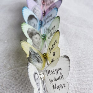Silk butterfly wedding keepsake pins all lined up on a linen cloth. The delicate  pastel colours like a subtle rainbow. each one customised with an image and words of your choice