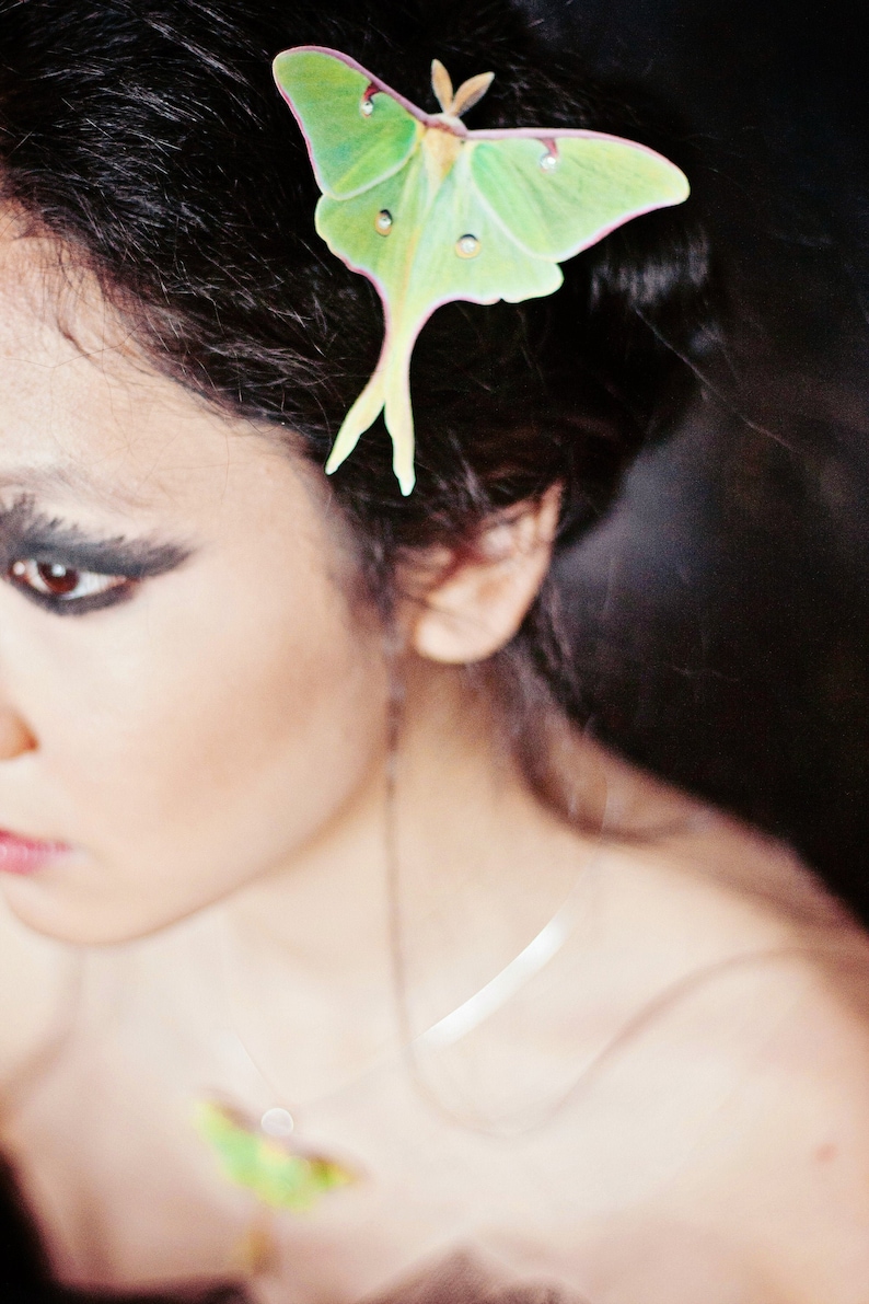 A model with black smoky eyes and black hair wears a pale green luna moth hair clip with crystal details