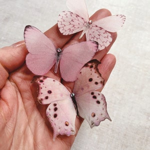 A hand holds a set of 3 pale pink silk butterflies in different shapes. Each one has been carefully hand cut from fine silk and has a tiny sparkling crystal on its head. Pretty summer wedding accessories