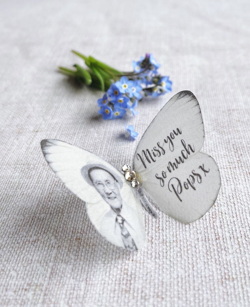 A little white silk butterfly brooch has been personalised with an image of an old man on the opposite wing are the words Miss you so much Pops x