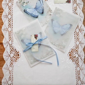 A flat lay image of three silk butterfly hair clips in their pretty gift packaging. They are sent on vintage style glossy postcards tucked into vellum envelopes and tied with satin ribbon.