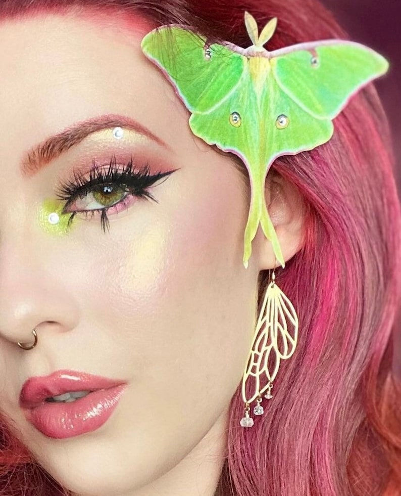 A lady with red hair and beautifully applied make up wears a silk luna moth hair clip with crystal details