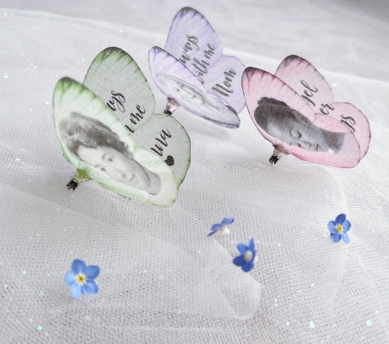 Three pretty silk butterfly pins, one pale green, one lilac and one pale pink. each little butterfly has been personalised with an image of a person and have custom text in a cursive font on their wings