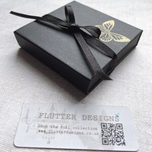 A little black gift box tied with ribbon and stamped with a gold butterfly.