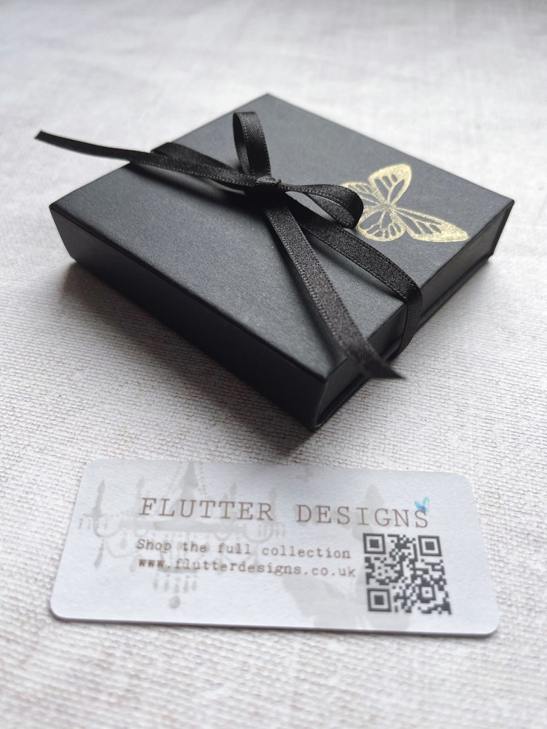 A little black gift box tied with ribbon and stamped with a gold butterfly.