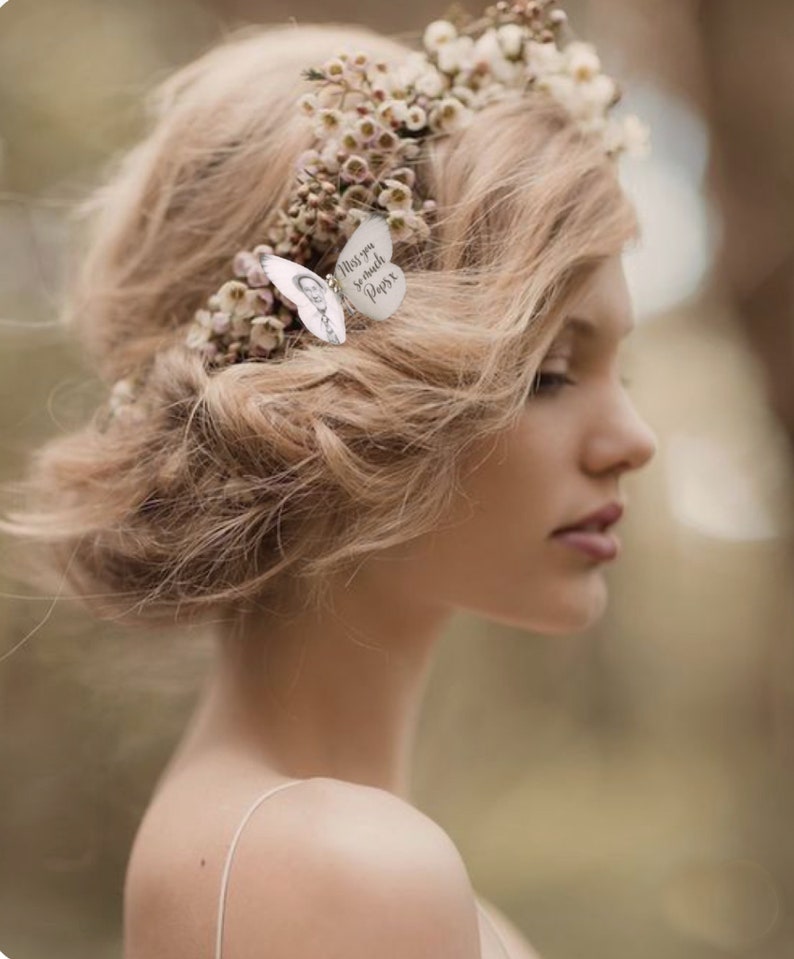 A bride wears a floral crown with a silk butterfly hair pin personalised with a photo of a man and the text "Miss you so much Papa" in her hair.