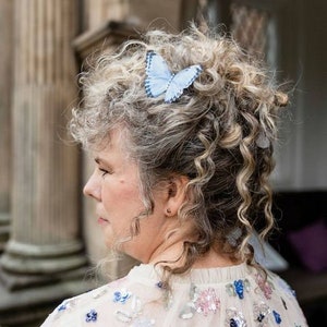 A bride wears a beautiful sequinned cape, in her curl hair she wears a blue silk butterfly with a crystal encrusted body