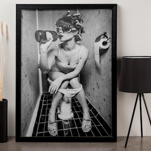 Puede incluir: Fotograf&iacute;a en blanco y negro de una persona sentada en un inodoro, con gafas de sol y bebiendo de una botella. La persona tiene el pelo en rulos. Un rollo de papel higi&eacute;nico cuelga de la pared detr&aacute;s de ella.