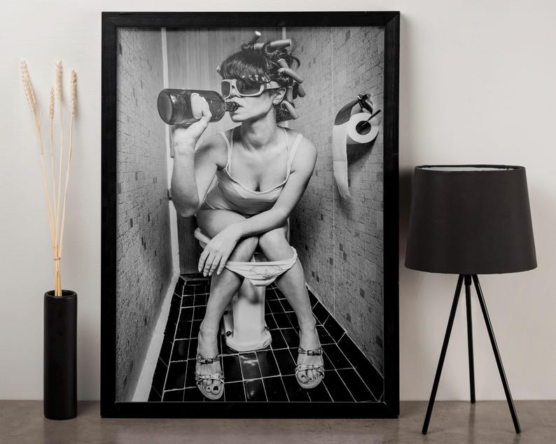 Puede incluir: Fotograf&iacute;a en blanco y negro de una persona sentada en un inodoro, con gafas de sol y bebiendo de una botella. La persona tiene el pelo en rulos. Un rollo de papel higi&eacute;nico cuelga de la pared detr&aacute;s de ella.