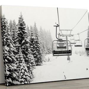 May include: Black and white photograph of a ski lift in a snowy forest. The lift is carrying empty chairs up the mountain. The trees are covered in snow and the sky is overcast.