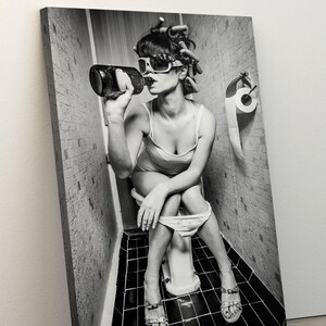 Puede incluir: Una foto en blanco y negro de una persona sentada en un inodoro en un ba&ntilde;o. La persona lleva gafas de sol y tiene el pelo en rulos. Est&aacute; sosteniendo una botella y bebiendo de ella.