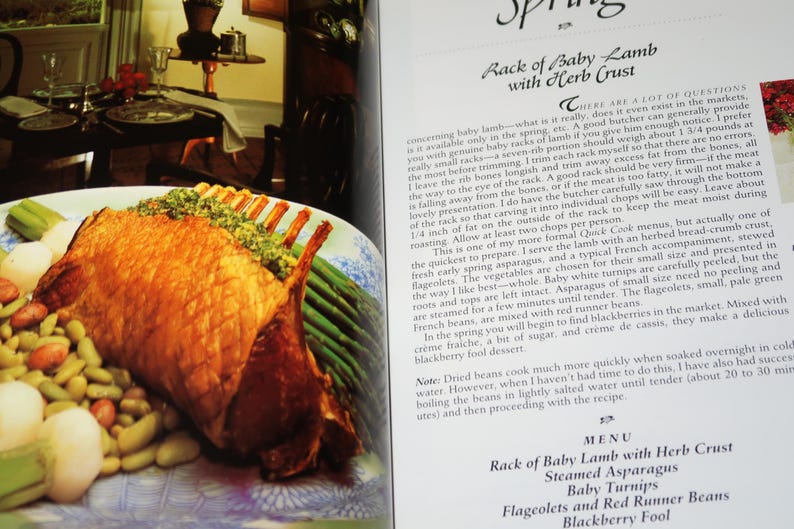 May include: A close-up of a roasted rack of baby lamb with a herb crust, served with steamed asparagus, baby turnips, flageolet beans, and red runner beans. The dish is presented on a white and blue patterned plate. The text "Rack of Baby Lamb with Herb Crust" is visible in the bottom right corner of the image.