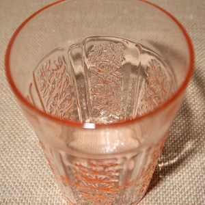 May include: A clear pink glass tumbler with a floral pattern. The glass has a slightly rippled texture and a rounded bottom.