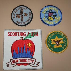 Puede incluir: Cuatro parches bordados con diferentes diseños. El parche superior izquierdo es azul con texto blanco que dice "Blue Elk District Webelos Woods 1983". El parche superior derecho es azul con texto amarillo que dice "Marin Council Klondike Derby". El parche inferior izquierdo es blanco con bordados rojos, azules y amarillos que dicen "Scouting / USA New York City". El parche inferior derecho es verde con texto amarillo que dice "Assistant Senior Patrol Leader".