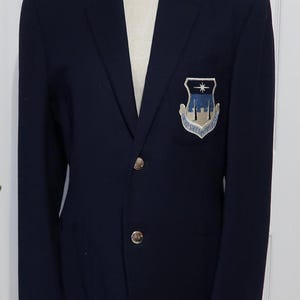 May include: A navy blue blazer with a patch on the left breast featuring a white star, a blue and white building, and the text "United States Air Force".