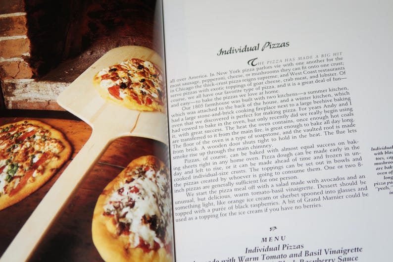 May include: A close-up of a cookbook page with a recipe for individual pizzas. The page features a photo of several pizzas with different toppings, including cheese, pepperoni, and vegetables. The text on the page describes the history of pizza and how to make it at home.