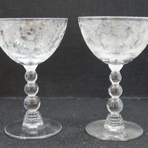 May include: Two clear glass champagne coupes with a floral etched design and a beaded stem.