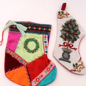 May include: Two Christmas stockings. One is patchwork with a green wreath, the other is white with a tree design. The patchwork stocking has a green bow and is made of various colors including pink, red, and orange.