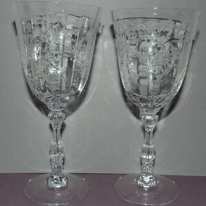 May include: Two clear glass wine glasses with etched floral designs and a fluted bowl. The glasses have a decorative stem with a knob at the base.