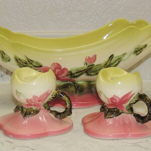 May include: A set of three vintage ceramic candle holders. The center piece is a large, green and white bowl with floral designs. The two smaller pieces are candle holders with pink bases and white candle cups with floral designs.
