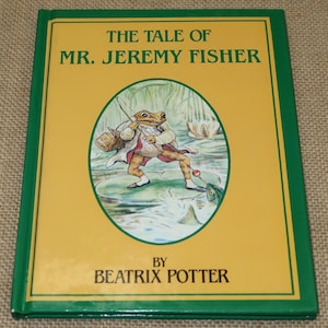 May include: A hardcover book titled "The Tale of Mr. Jeremy Fisher" by Beatrix Potter. The cover features a yellow background with a green border. An illustration depicts a frog fishing with a basket and a fishing rod.