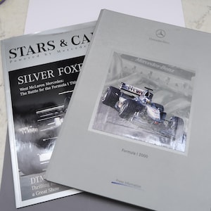 Puede incluir: Dos revistas sobre carreras de Fórmula 1. La portada de la revista de la izquierda presenta un coche de carreras plateado y el texto "STARS & CARS Powered by Mercedes SILVER FOXE West McLaren Mercedes: The Battle for the Formula 1 Title". La portada de la revista de la derecha presenta un coche de carreras plateado y el texto "Mercedes-Benz Formule 1 2000".